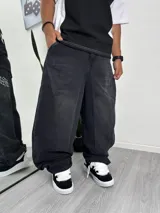 Pantalón de jean negro lavado, corte muy ancho (baggy) con estampado vertical en blanco con tipografía gótica en el lateral de la pierna.