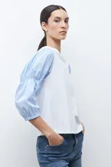 Remera de manga corta con cuerpo blanco liso y mangas largas abullonadas de tela a rayas celestes y blancas.