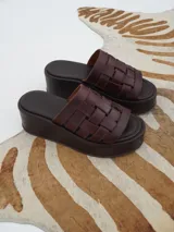 Sandalias marrones de cuero con plataforma pareja. Diseño con tiras de cuero tejidas en la parte superior y suela ancha que aporta estabilidad y comodidad.