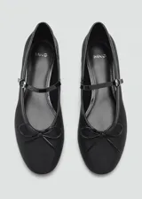 Zapato tipo ballerina color negro con puntera redondeada, tira sobre el empeine con hebilla y moño decorativo.