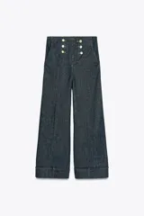 Pantalón culotte de tiro alto en denim azul oscuro, con pernera ancha y corta terminada en vuelta. Presenta falsos botones dorados en la parte delantera, bolsillos frontales y cierre con cremallera y gancho.