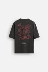 Camiseta negra con cuello redondo y mangas cortas. Estampado frontal con la frase "Cherry Pill Blush Delight" y una ilustración de una mujer en un cohete. Tiene un efecto de lavado que le da una apariencia única.