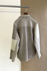 Camisa de hombre estilo leñadora con diseño patchwork en tonos beige y marrón. Presenta coderas, cartera americana y bolsillo ojal en el delantero. Confeccionada en lana fina sin teñir.