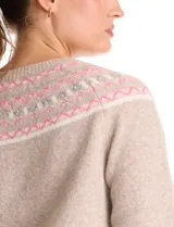 Buzo de punto color beige, con cuello a la base y silueta clásica de hombros relajados. Presenta una guarda tejida con motivos geométricos en tonos rosados, blancos y grises en el canesú. Puños y ruedo con acabado acanalado.