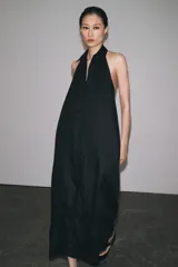 Vestido midi negro de lino, con cuello halter, hombros descubiertos, espalda descubierta, cierre frontal con botones y bajo asimétrico.