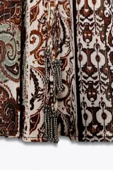 Vestido corto con estampado de cachemira en tonos marrones, beige y verde. Tiene escote en pico con abalorios, mangas cortas y cintura elástica con cinturón fino.