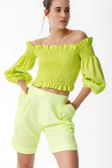 Crop top color verde lima, con escote off-shoulder con volados y mangas 3/4 abullonadas. El torso presenta punto panal elastizado.