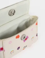 Monedero de cuerina color crudo con estampado de motivos japoneses y la palabra "Tokyo". Tiene forma de bolso con manija superior, solapa con broche a presión y mosquetón lateral.