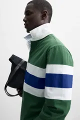 Polo de rugby verde con rayas horizontales azules y blancas, cuello blanco con solapa y cierre de botones, y mangas largas con puños acanalados.