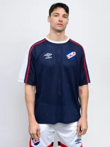 Remera de fútbol Umbro del Club Nacional de Football, color azul marino con detalles en blanco y rojo. Diseño de mesh con cortes, cambio de color y piping.