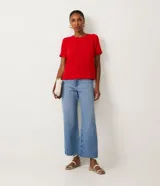 Blusa blanca de poliéster con cuello redondo, mangas cortas, cierre trasero en forma de gota, pequeñas aberturas laterales y acabados en pespuntes en las mangas y el cuello.