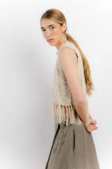 Chaleco de hilo color crema, con cuello redondo y diseño calado. Presenta flecos en el ruedo.