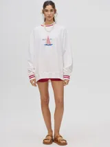 Buzo blanco de corte redondo (crew neck) con puños ajustados que tienen rayas rojas y blancas. Presenta un estampado central de un velero navegando con texto alrededor.