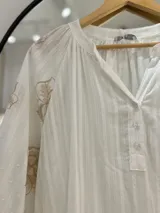 Blusa blanca con escote en pico y botones en el frente. Detalles florales bordados en mangas.