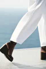 Sandalias negras con plataforma de madera, tacón de cuña y tira delantera con detalle de tachas doradas. Cierre mediante tira con pulsera al tobillo y acabado en punta cuadrada.