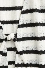 Top sin mangas de punto fino a rayas horizontales blancas y negras, con escote en V y cierre con lazo en el centro. Ribete festoneado en sisas y cuello.