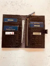 Billetera porta pasaportes de cuero sintético color marrón con textura tipo cocodrilo. Cuenta con cierre de broche y cierre de cremallera, múltiples ranuras para tarjetas y compartimentos para pasaportes y billetes.
