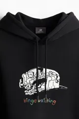 Canguro negro de corte regular con capucha ajustable con cordón, bolsillo tipo canguro y puños y bajo acanalados. Estampa frontal con dibujo de personas mirando televisión y la frase "binge watching" en letras de colores.