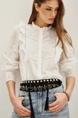 Cinturón ancho tipo faja de cuero negro, con tachas metálicas redondas y detalles de apliques en forma de onda o zigzag. Posee cordones de ajuste con borlas colgantes en los extremos.