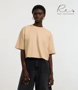 Blusa color beige, cropped y de corte amplio, confeccionada en tejido de media malla, con cuello redondo y mangas cortas.