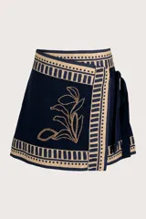 Minifalda azul marino con estampado floral dorado, corte asimétrico y lazo lateral.
