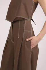 Pantalón negro de tiro alto, corte ancho y largo, con pliegues frontales y pespuntes contrastantes en blanco en la cintura y bolsillos.