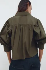 Camisa color verde oliva de popelina de algodón, con cuello solapa, manga corta abullonada y cierre frontal con botones.