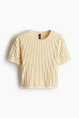 Top color crema en tejido de punto trenzado, con cuello redondo y mangas cortas con ribete blanco.