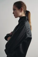 Sobrecamisa negra de efecto piel, con cuello de solapa, manga larga con puños abotonados, bajo recto y cierre frontal con botones.