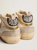 Zapatillas de media caña Golden Goose modelo Mid Star, color blanco con detalles en beige y gris. Presentan una estrella de gamuza rosada en el lateral, perforaciones decorativas y efecto desgastado en la suela.