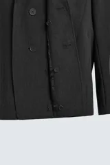 Blazer negro de corte relajado con cuello de solapa de muesca desmontable, manga larga, bolsillos frontales ocultos y cierre frontal con botones.