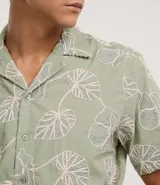 Camisa de calce comfort de la marca Marfinno, confeccionada en algodón color verde con bordado de hojas blancas. Posee cuello con solapa, manga corta y cierre frontal con botones.