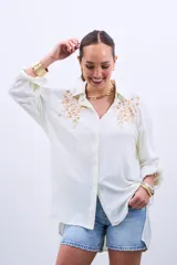 Camisa color crudo con bordado de lentejuelas doradas en el frente, de corte holgado y mangas largas con lazo en los puños.
