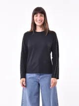 Remera negra de manga larga con cuello redondo y detalle de tachas plateadas en las mangas.