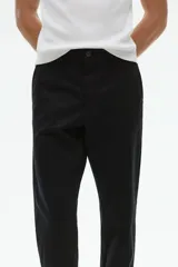 Pantalón negro de corte slim fit, confeccionado en sarga elástica de algodón. Cuenta con cierre y botón, bolsillos al bies y bolsillos insertados atrás con botón.
