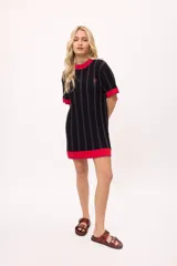 Vestido de tejido de punto, color negro con rayas verticales grises. Tiene cuello redondo y puños y ruedo en color rojo con costuras decorativas en hilo azul. Presenta un pequeño bordado de una letra 'B' estilizada en el pecho.