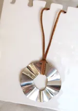 Colgante plateado con forma circular ondulada y tira de cuero marrón.