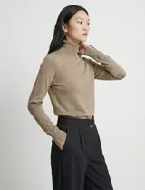 Polera de punto fino marca Nienty, color blanco, con cuello alto volcado y mangas largas con detalle de tajo en los puños.