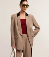 Blazer de tejido plano color beige con estructura de sastrería, cuello smoking con contraste negro en la nuca, botón único para cierre y solapas delanteras que simulan bolsillos.