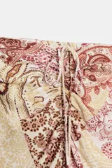 Falda midi de tiro alto con estampado paisley en tonos beige, rosa y marrón. Presenta frunces y cordón lateral, abertura en el bajo y cierre lateral con cremallera oculta.
