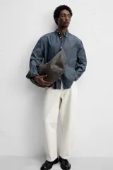 Camisa azul de algodón con textura chambray, corte regular fit, cuello abotonado, manga larga con puños abotonados, bolsillo de parche en el pecho y cierre frontal con botones.