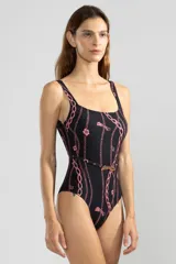 Traje de baño enterizo negro con estampado de cadenas y tigres rosas. Tiene escote cuadrado, breteles anchos y cinturón blanco con hebilla dorada en forma de tigre.