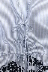 Blusa de rayas verticales azules y blancas, con escote en pico, mangas cortas abullonadas con elástico y bajo con bordados florales perforados. Cierre frontal con lazos.