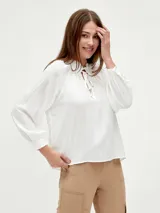 Blusa blanca de mangas largas con cuello fruncido y lazo.
