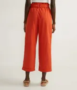 Pantalón clochard color naranja, con cintura elástica, cinturón para atar, cierre por cremallera, pliegues delanteros y barra doblada.