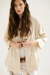Sobrecamisa beige de corte recto, cuello mao y mangas 3/4. Presenta cierre frontal con botones de madera y bolsillos laterales.
