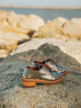 Zapato acordonado color bronce de cuero vacuno con perforaciones decorativas, taco de madera con folia en cuero de 4cm y entre suela de goma de 1,5cm. Horma de punta redonda y cómoda.