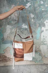 Cartera de cuero vacuno en colores camel, blanco y cobre, con manija corta y correa larga ajustable.