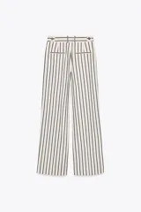 Pantalón de tiro medio con estampado de rayas verticales negras sobre fondo blanco. Tiene trabillas en la cintura, bolsillos laterales, pinzas delanteras y cierre frontal con cremallera, botón y ganchos metálicos.