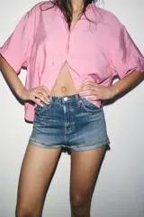 Shorts de jean de algodón, tiro alto, color azul claro desgastado. Presenta cinco bolsillos, cierre frontal con botón metálico y bajo desflecado con vuelta.